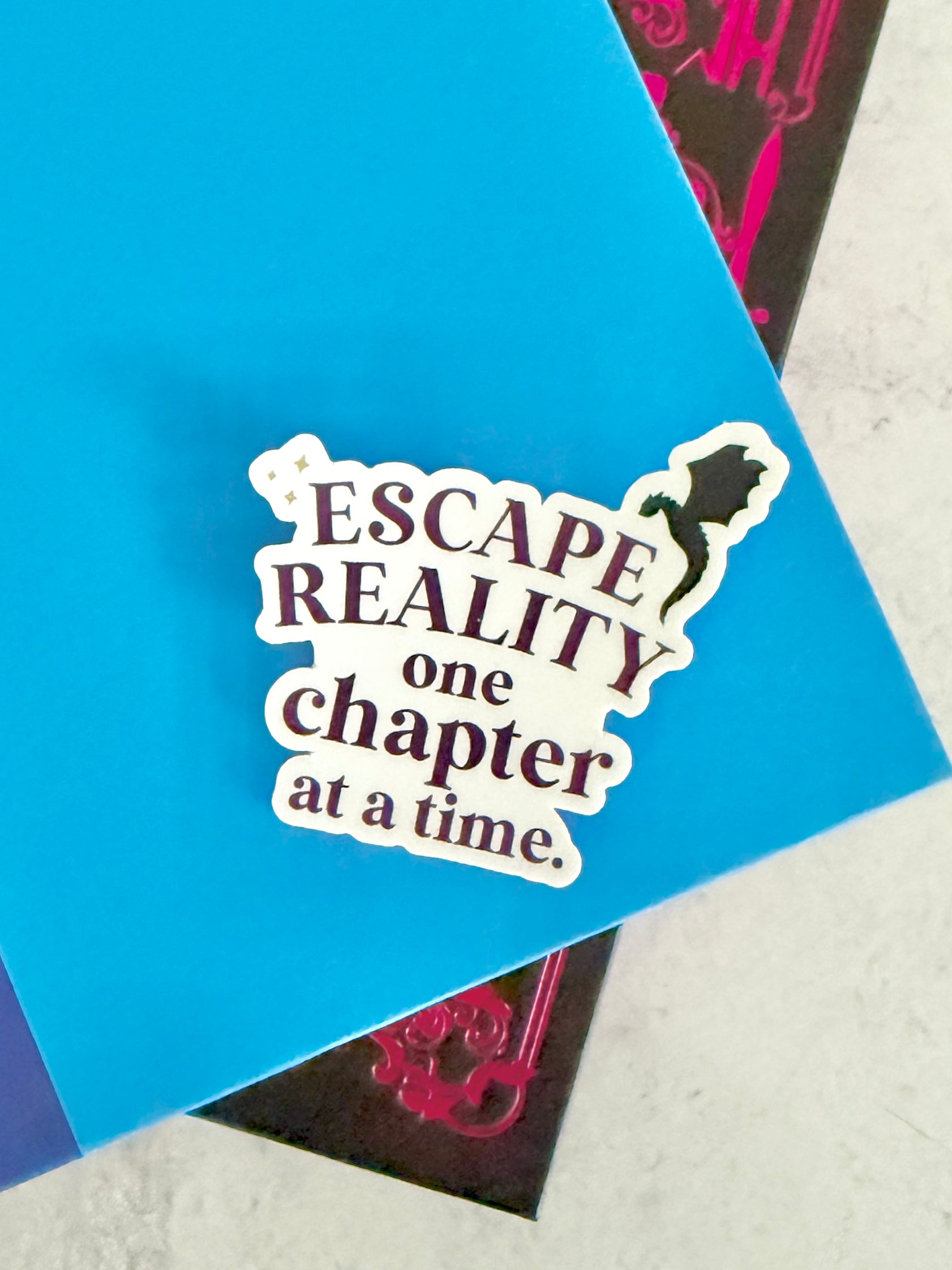 Escape Reality One Chapter at a Time vinyl sticker with dragon silhouette and purple typography on a stack of books