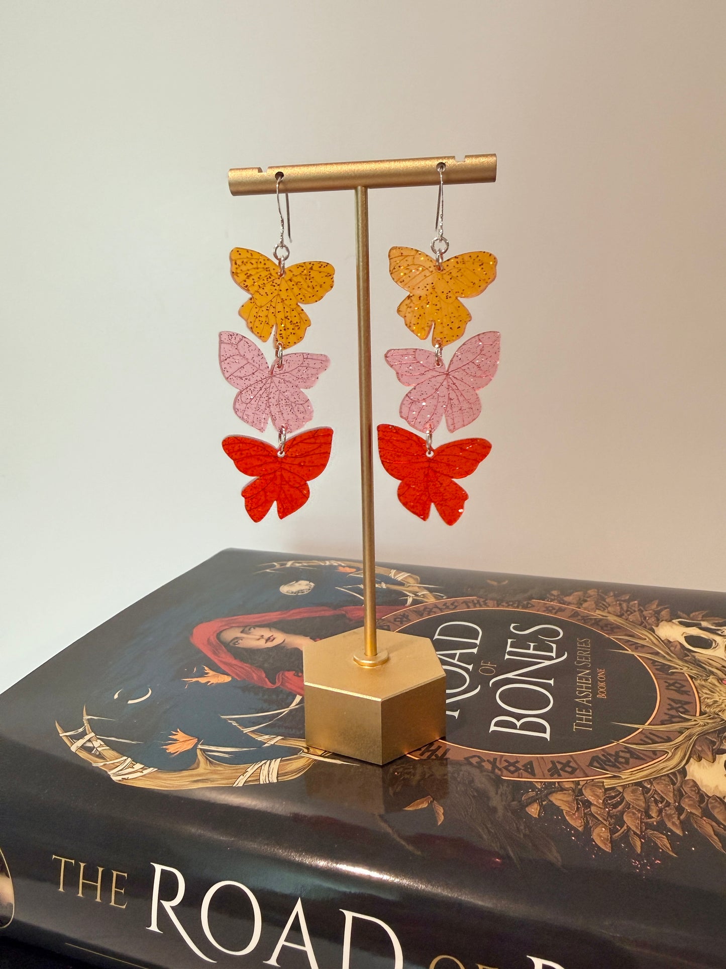 Butterfly-shaped earrings on a stand with a Road of Bones book by Demi Winters in the background