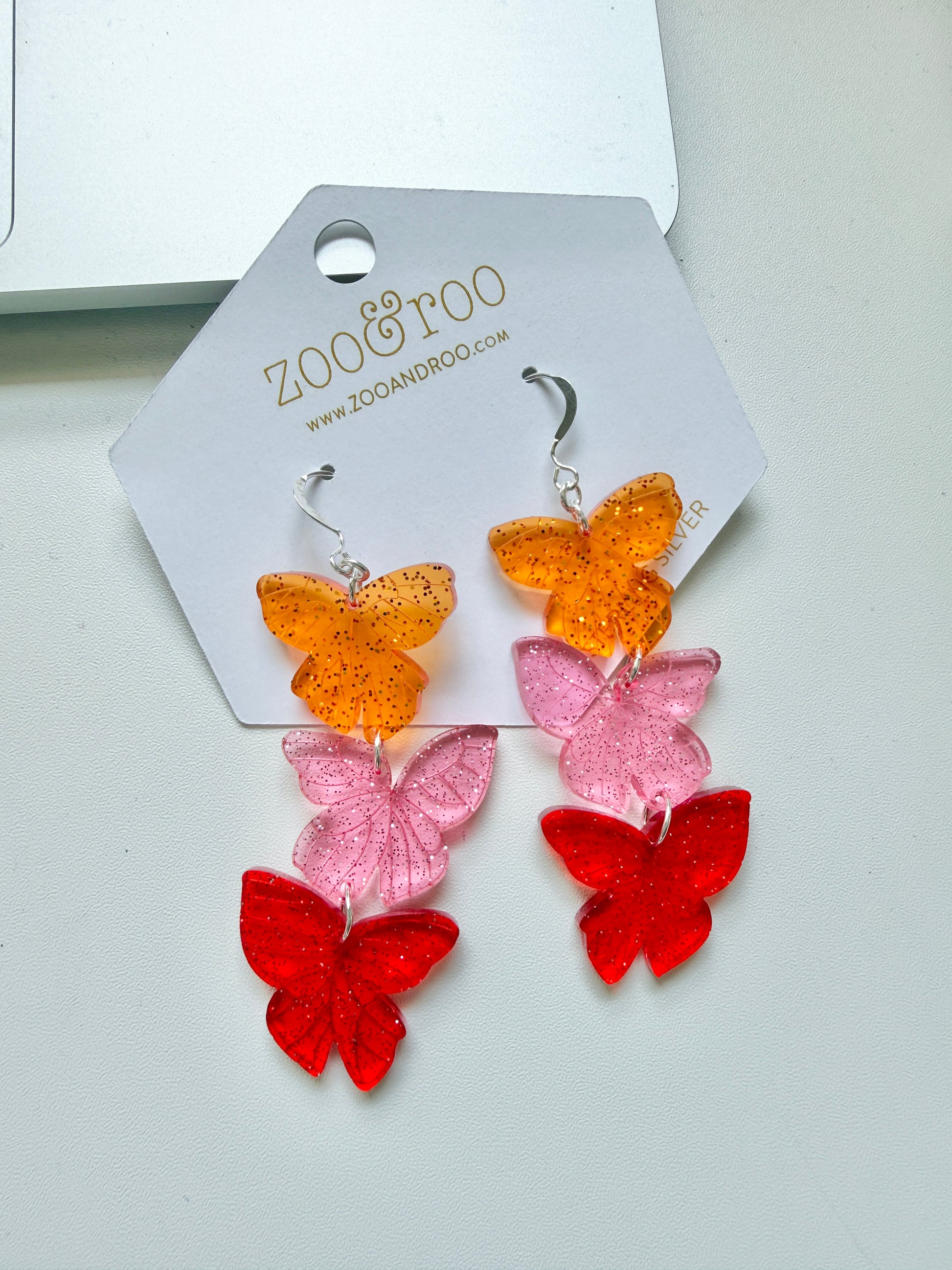 Flíta butterfly earrings inspired by Road of Bones by Demi Winters on a display card with zoo&roo branding, against a white background.