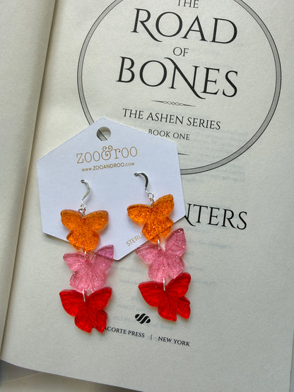 Flíta butterfly earrings on a 'The Road of Bones' book by Demi Winters with zoo&roo branding.