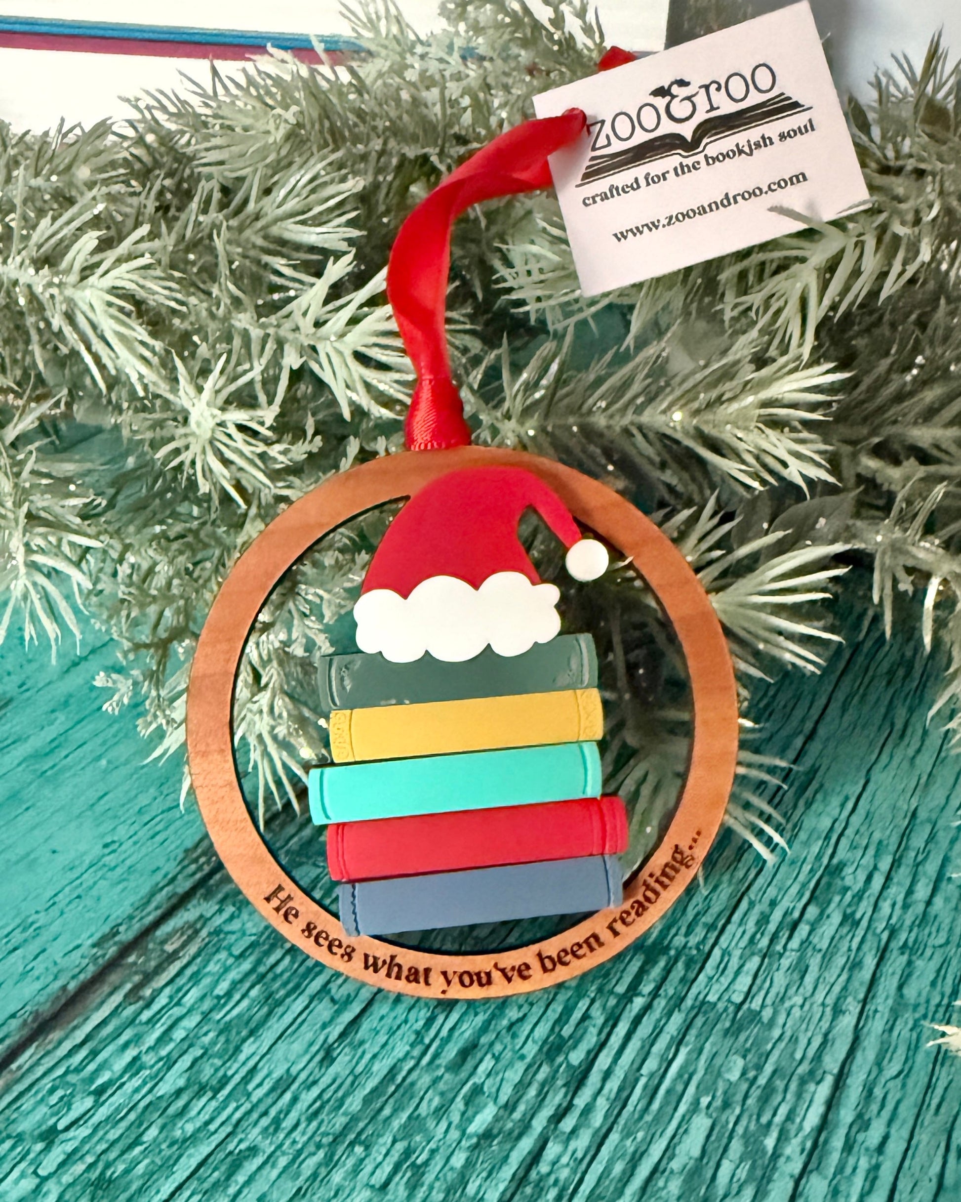 Bookish Christmas ornament with books and Santa hat engraved with "he sees what you've been reading"