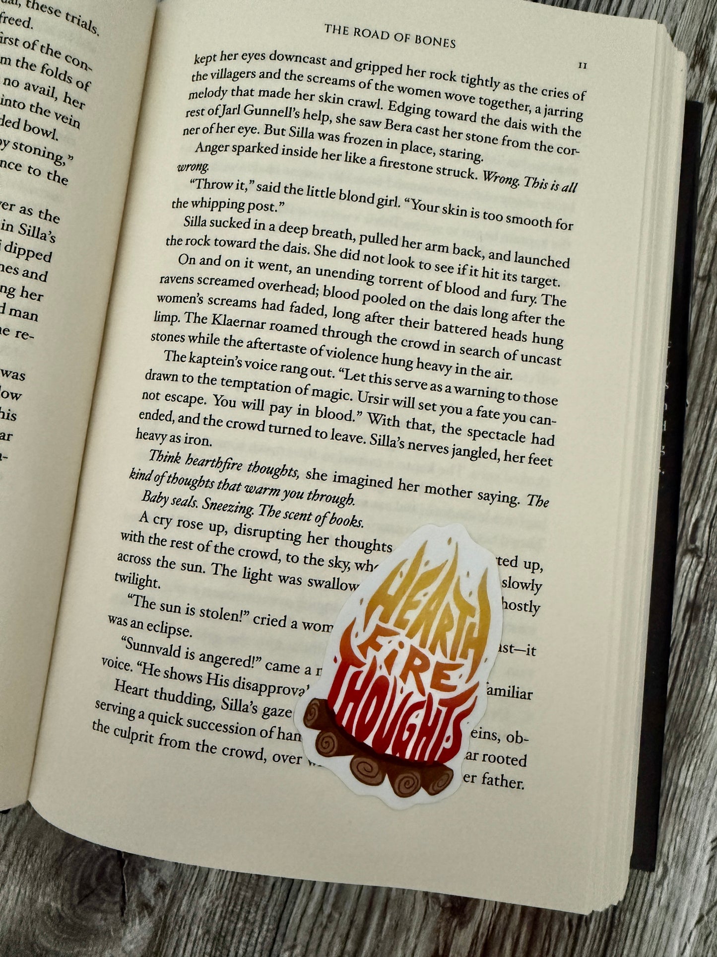 Open book with a sticker featuring flames and the text 'Hearth Fire Thoughts' inspired by Demi Winters' The Road of Bones.