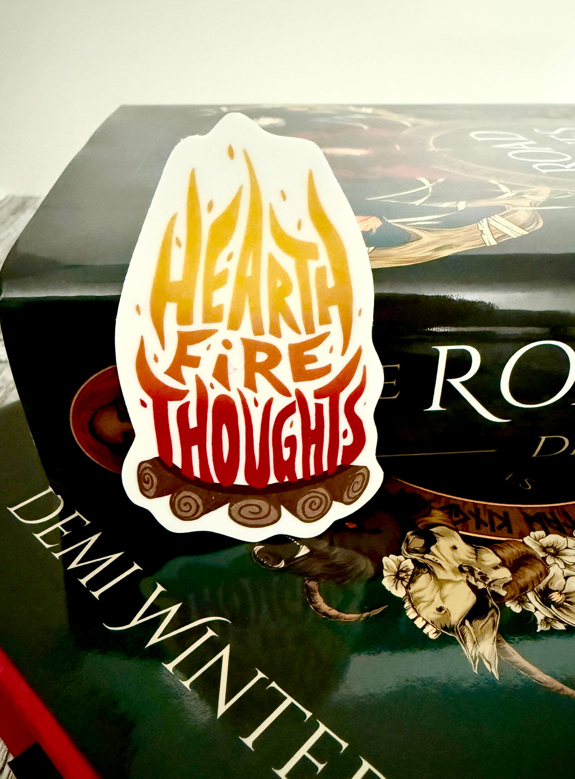 Sticker with 'Hearthfire Thoughts' text on a book titled 'The Road of Bones' by Demi Winters.