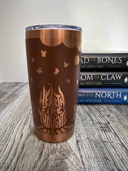 Brown tumbler with 'Heart Fire Thoughts' design on a wooden surface with Demi Winters Road of Bones books in the background.