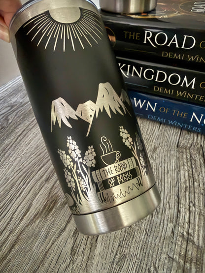 Black tumbler with engraved design inspired by Demi Winters' Ashen series, held over a stack of books.
