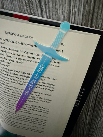 Sword-shaped bookmark with 'turn your pain into Power' text on a 'Kingdom of Claw' book by Demi Winters