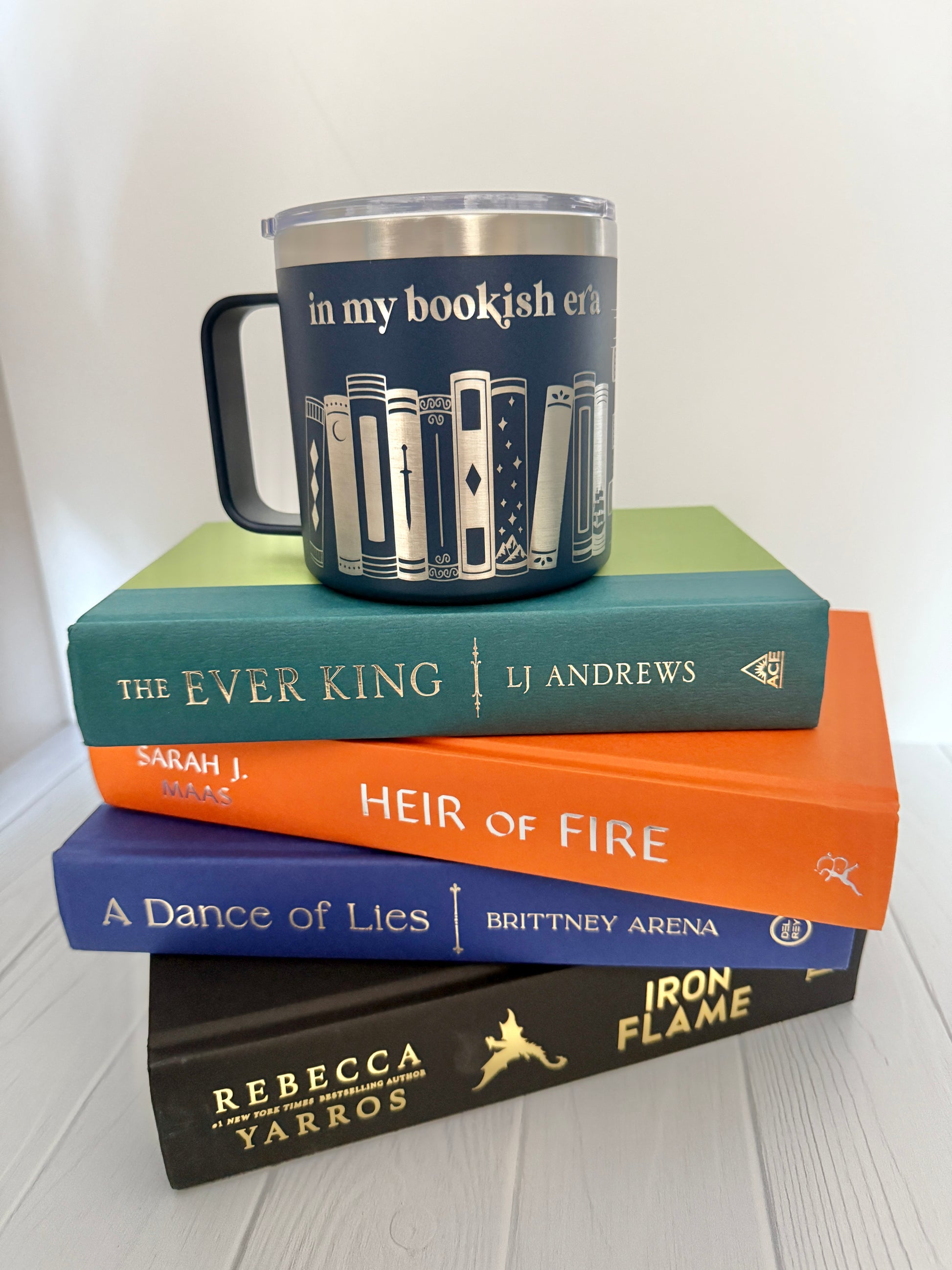 Stack of books with a mug engraved with 'in my bookish era' on a white surface