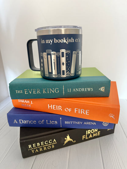 Stack of books with a mug engraved with 'in my bookish era' on a white surface