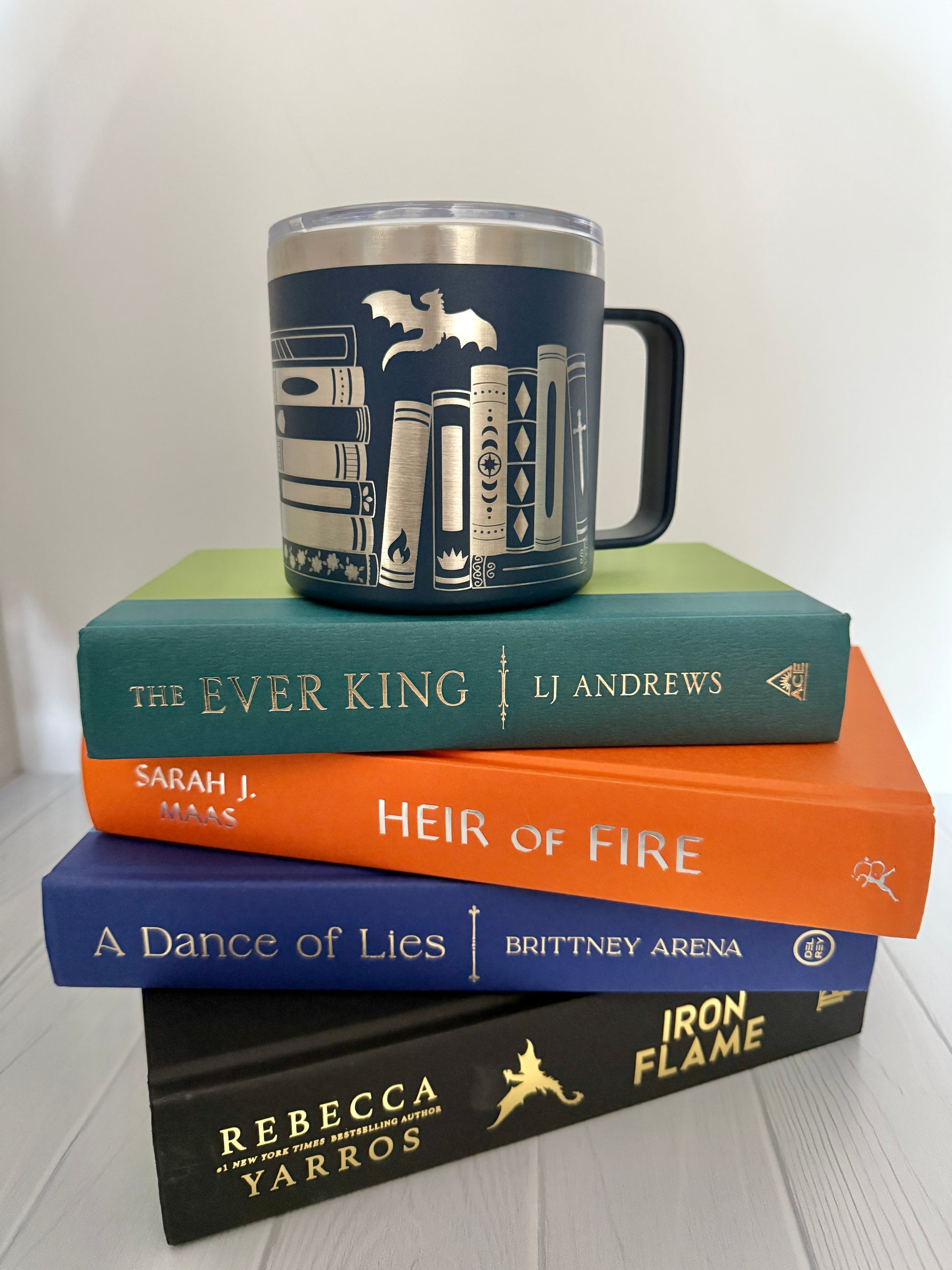 Stack of books with a mug on top engraved with books and a dragon against a white background