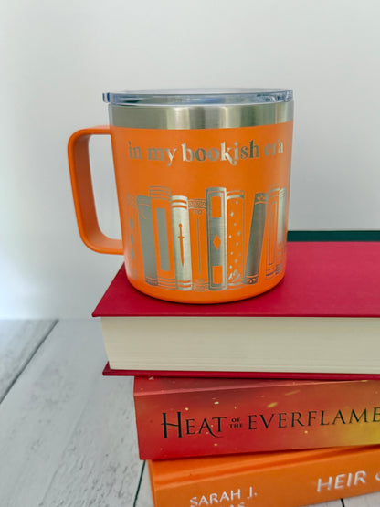 Orange stainless steel mug with 'in my bookish era' and books engraved around it, set on top of a stack of orange and red books.