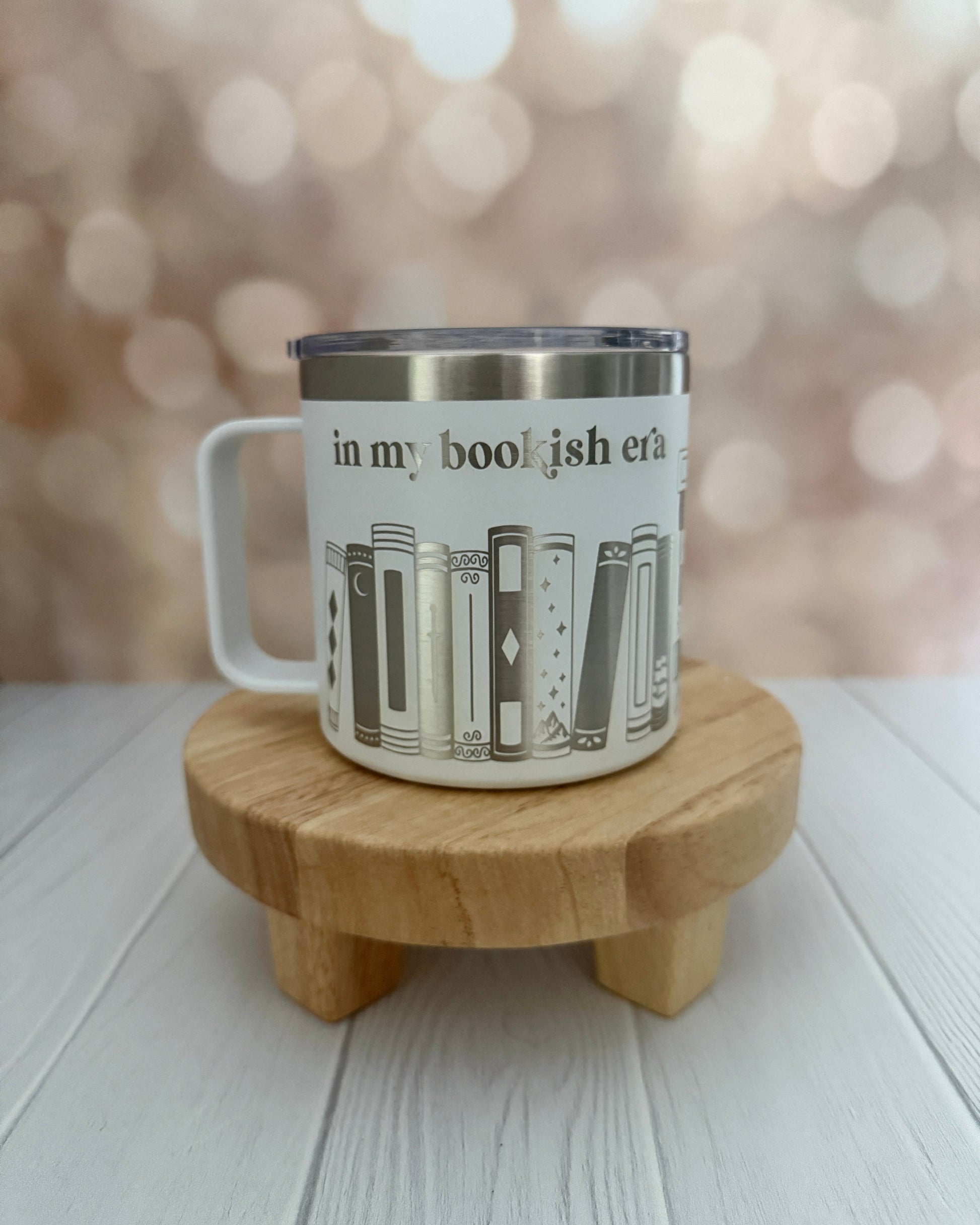 White mug with book design engraved 'in my bookish era' on a wooden stand with a blurred background