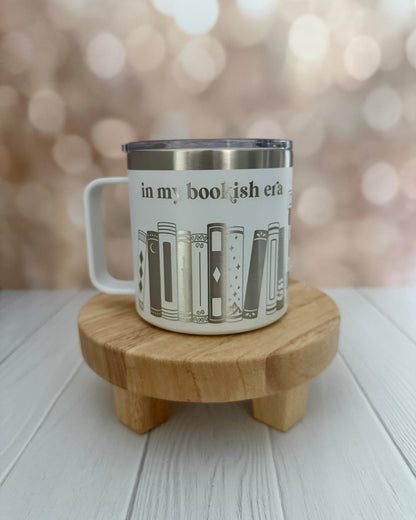 White mug with book design engraved 'in my bookish era' on a wooden stand with a blurred background