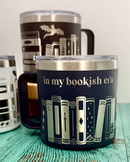 Mugs engraved with book design 'in my bookish era' on a wooden surface.