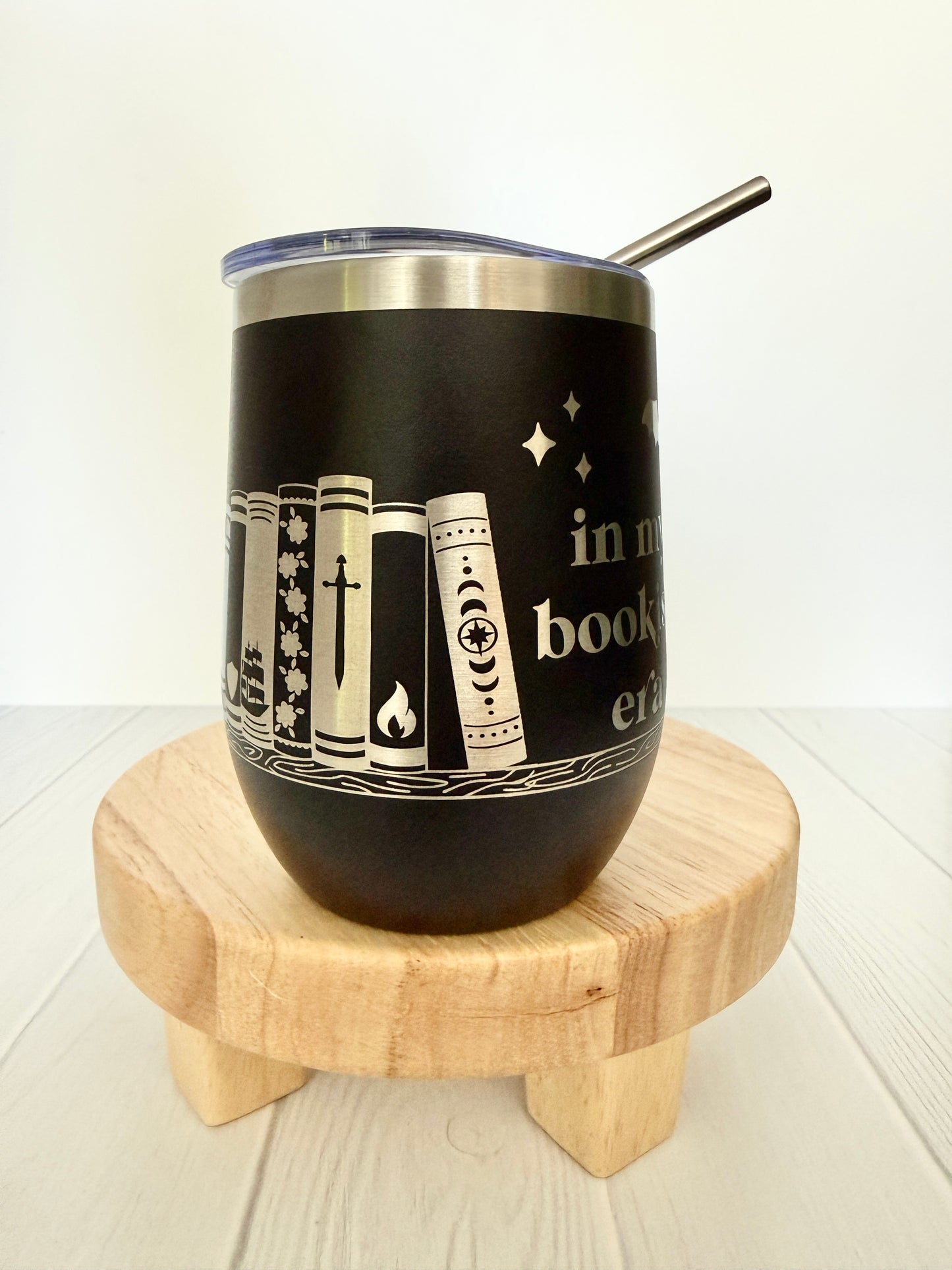 black wine tumbler spinning around, engraved with "in my bookish era" and books on a book shelf