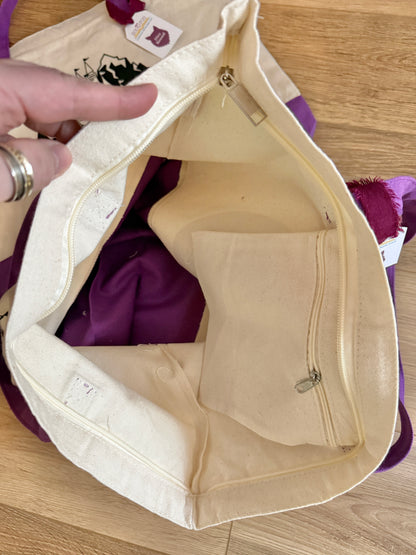 Looking inside a beige and purple tote bag with zippers and pockets on a wooden surface