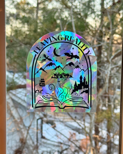 Holographic 'Leaving Reality' suncatcher decal on a window with blurred outdoor background