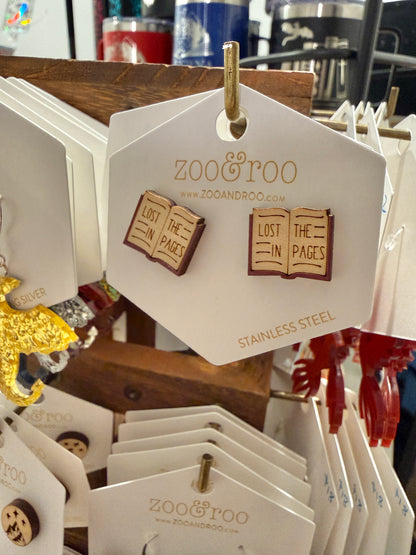 A pair of wood stud earrings shaped like an open book with the phrase 'LOST IN THE PAGES' displayed on a white zoo&roo branded hang tag.