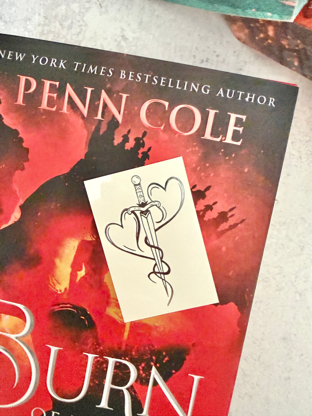 Two hearts forged into a dagger - the mating mark temporary tattoo resting on the cover of Burn of the Everflame by Penn Cole
