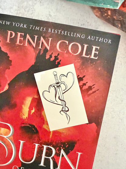 Two hearts forged into a dagger - the mating mark temporary tattoo resting on the cover of Burn of the Everflame by Penn Cole