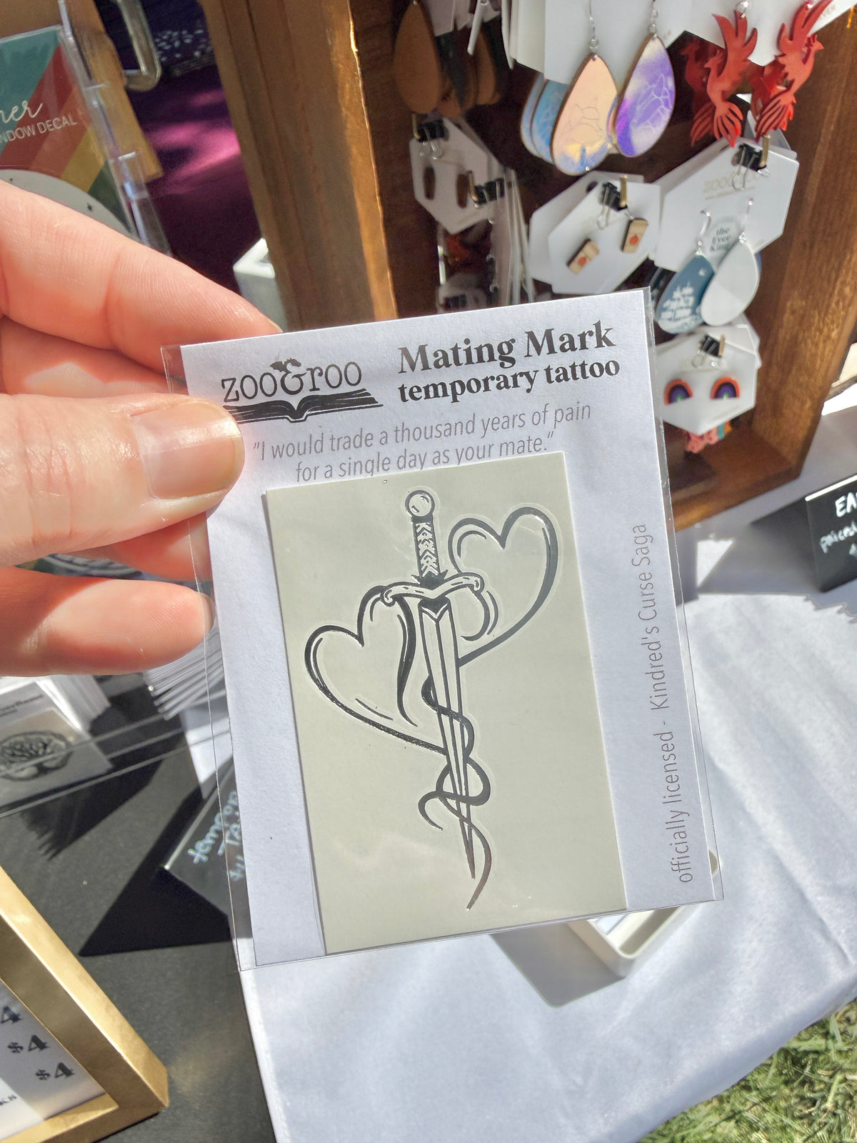 Hand holding the mating mark temporary tattoo package from the Kindred's Curse Saga at a zoo&roo market booth display
