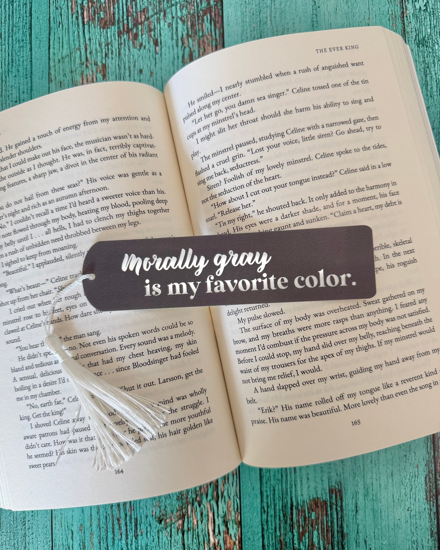 Open book with a bookmark that says 'Morally gray is my favorite color' on a wooden surface.
