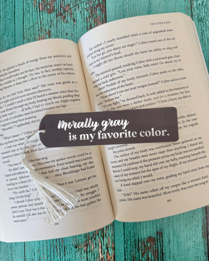 Open book with a bookmark that says 'Morally gray is my favorite color' on a wooden surface.