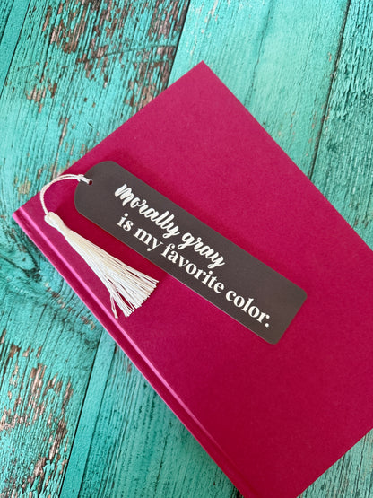 Red book with a gray bookmark that reads "morally gray is my favorite color" on a teal wooden surface