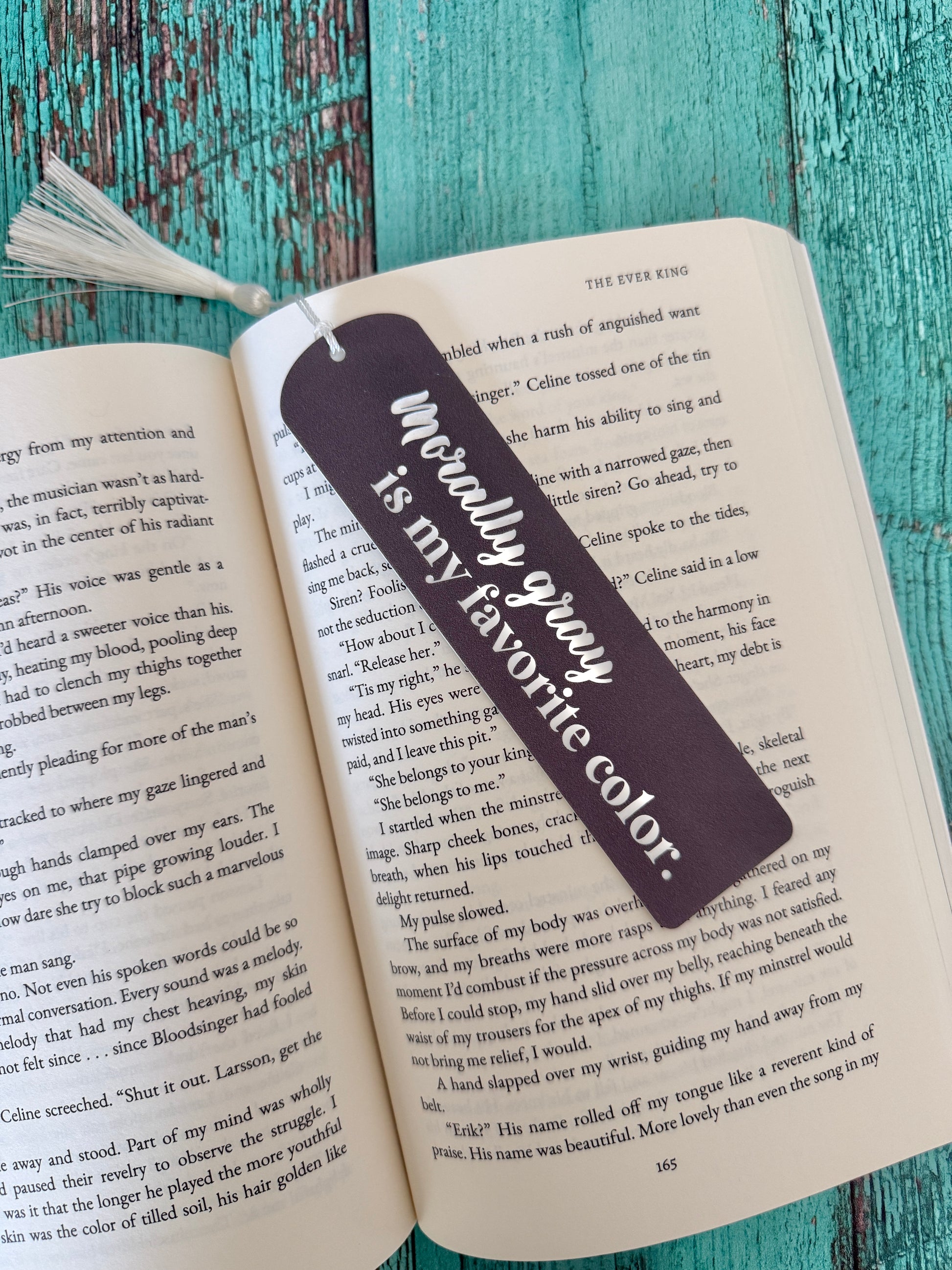 Bookmark with "morally gray is my favorite color" on an open book against a teal wooden background