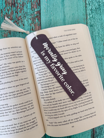 Bookmark with "morally gray is my favorite color" on an open book against a teal wooden background