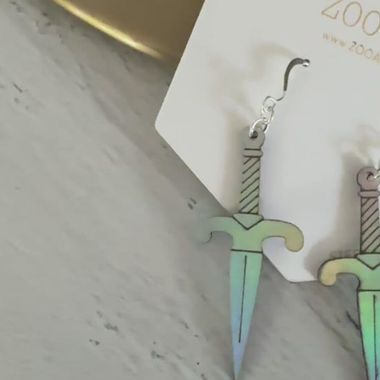 A pair of iridescent vegan leather dagger earrings, displayed on a white zoo&roo brand card against a light gray wood background.