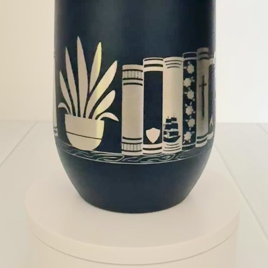 navy wine tumbler spinning around, engraved with "in my bookish era" and books on a book shelf with a dragon and stars