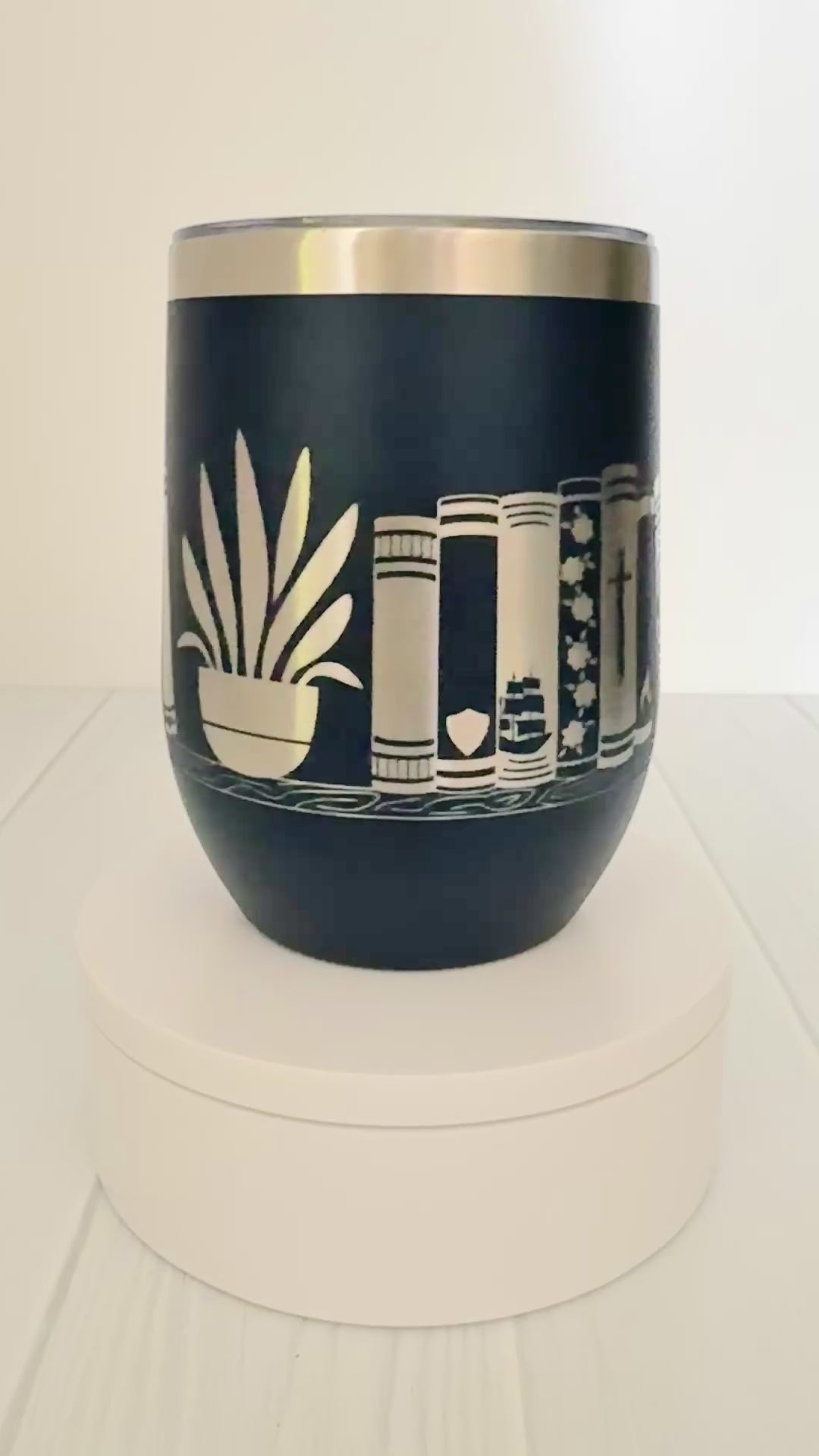 navy wine tumbler spinning around, engraved with "in my bookish era" and books on a book shelf with a dragon and stars