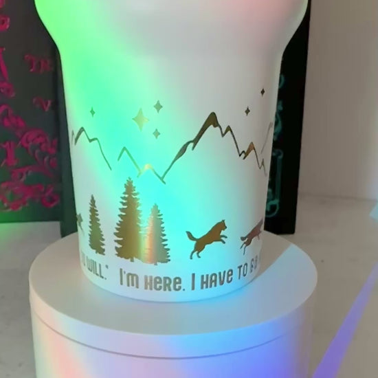 Closeup of a white 40 oz Dire Bound inspired tumbler with rainbow-engraved wolves running around the base of the tumbler with mountains, pine trees and stars and the quote 'you must, so you will.'