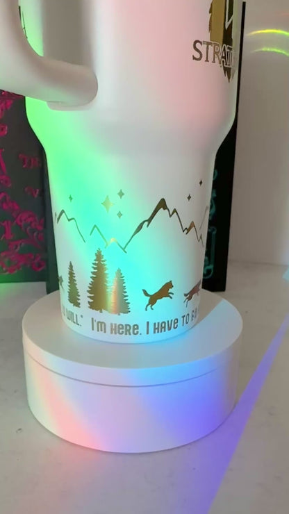Closeup of a white 40 oz Dire Bound inspired tumbler with rainbow-engraved wolves running around the base of the tumbler with mountains, pine trees and stars and the quote 'you must, so you will.'