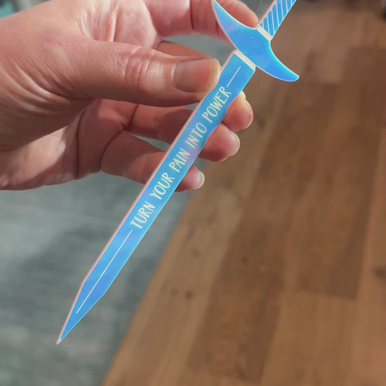 Iridescent acrylic sword shaped bookmark with 'turn your pain into power' engraved, inspired by Demi Winters' The Road of Bones book.