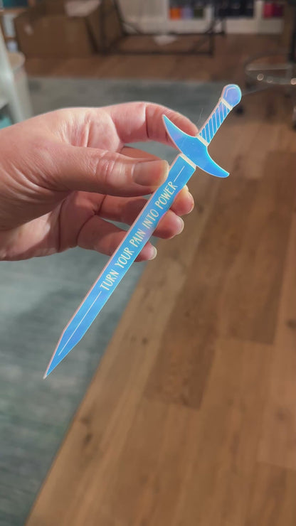Iridescent acrylic sword shaped bookmark with 'turn your pain into power' engraved, inspired by Demi Winters' The Road of Bones book.