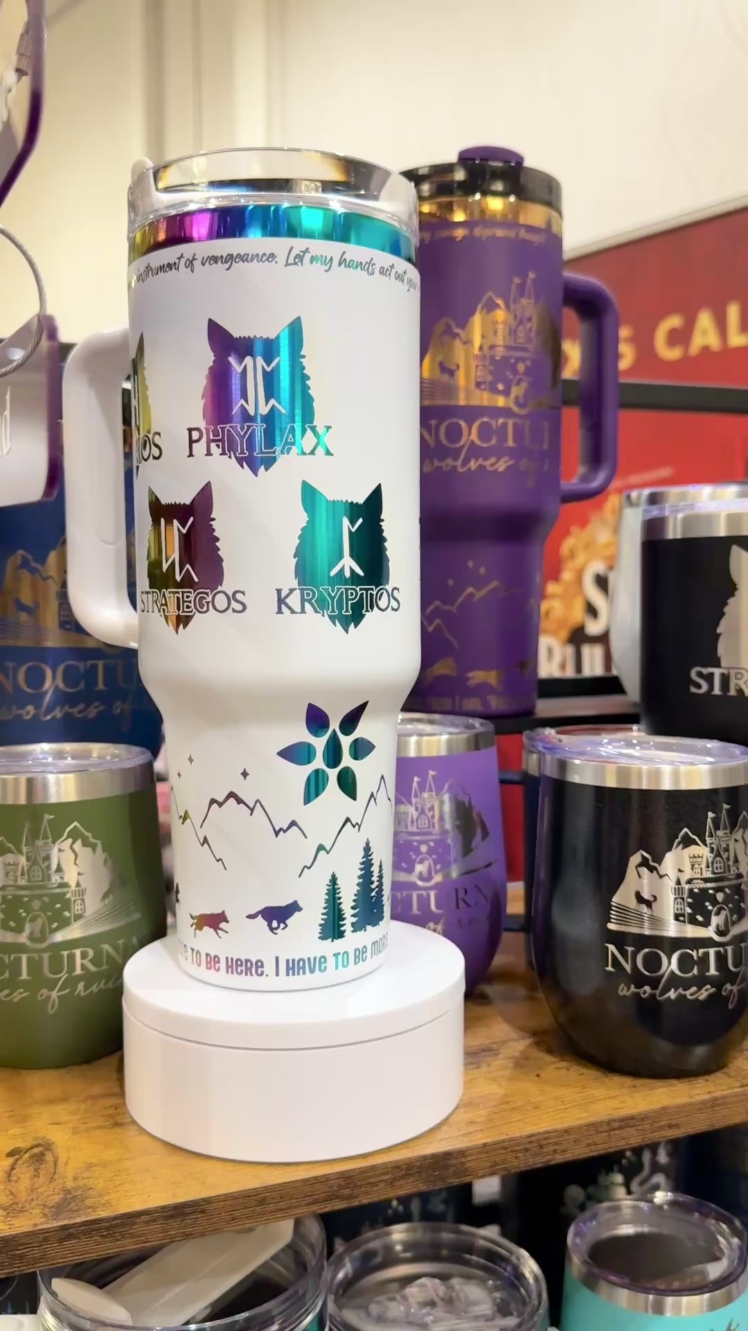 White 40 oz Dire Bound inspired tumbler with rainbow-engraved Nocturna castle, wolf pack symbols for Daemos, Phylax, Strategos and Kryptos, and wolves running around the base of the tumbler with mountains, pine trees and stars and the quote 'you must, so you will.'