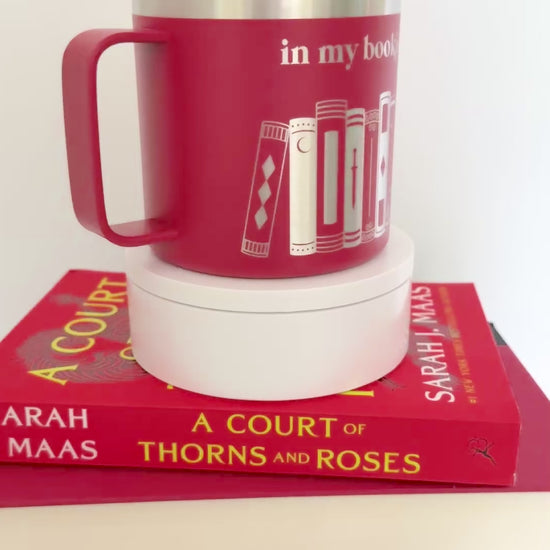 Red stainless steel mug with 'in my bookish era' and books engraved around it, set on top of a stack of red books.
