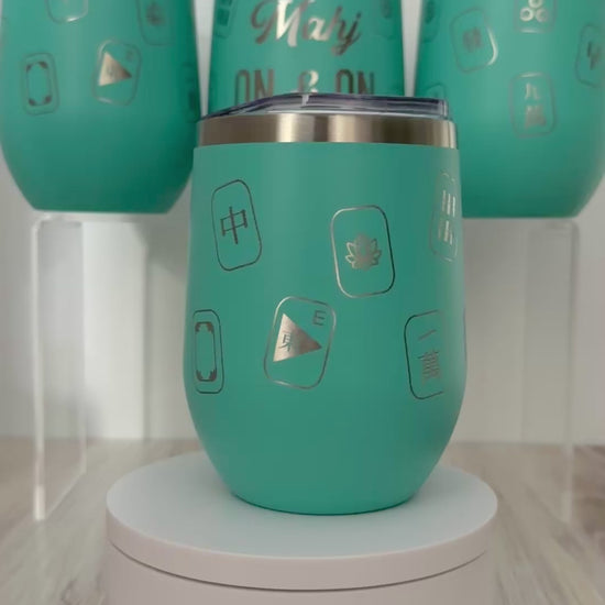 Mahjong wine tumbler with 'mahj on and on' text and mahjong tiles wrapped around the aqua tumbler.