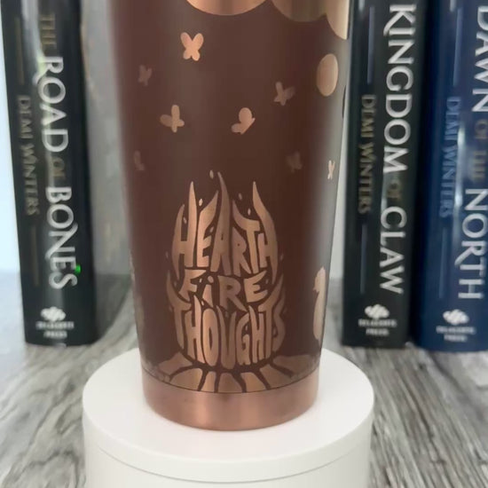 A brown and gold tumbler with 'Hearthfire Thoughts' design inspired by The Road of Bones Ashen series books by Demi Winters