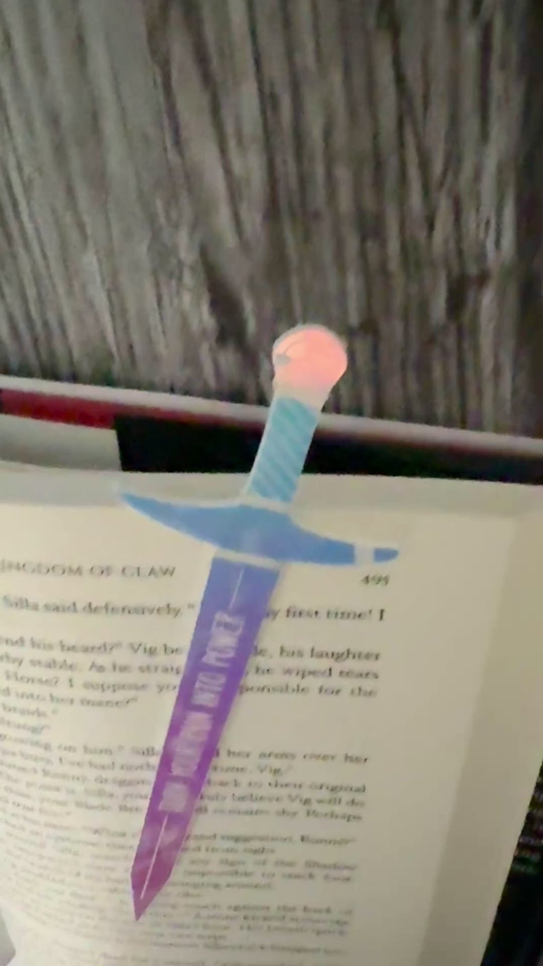 iridescent sword bookmark engraved with 'turn your pain into power' laying on an open book 'The Road of Bones' by Demi Winters