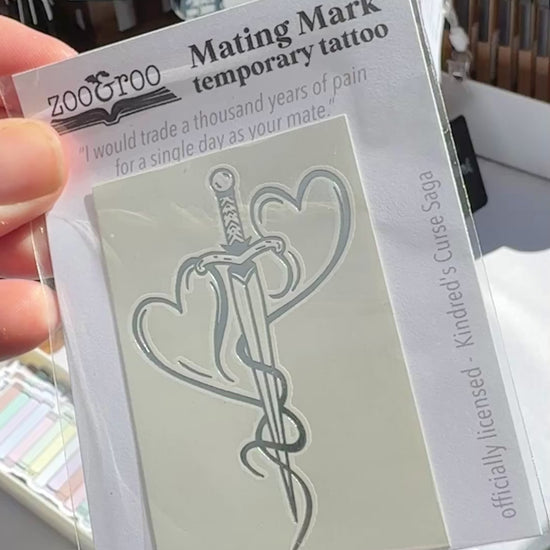 Hand holding the mating mark temporary tattoo package from the Kindred's Curse Saga at a zoo&roo market booth display
