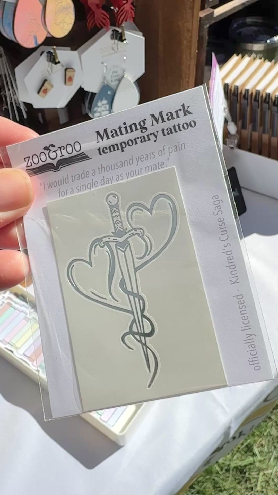 Hand holding the mating mark temporary tattoo package from the Kindred's Curse Saga at a zoo&roo market booth display