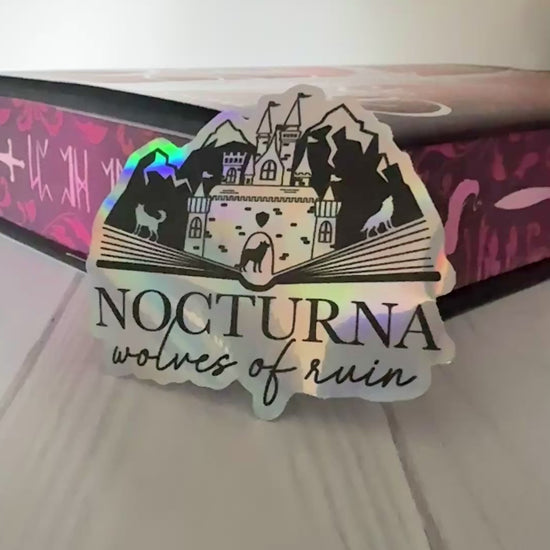 Nocturna holographic sticker featuring an open book with castle, mountains and wolves from Dire Bound