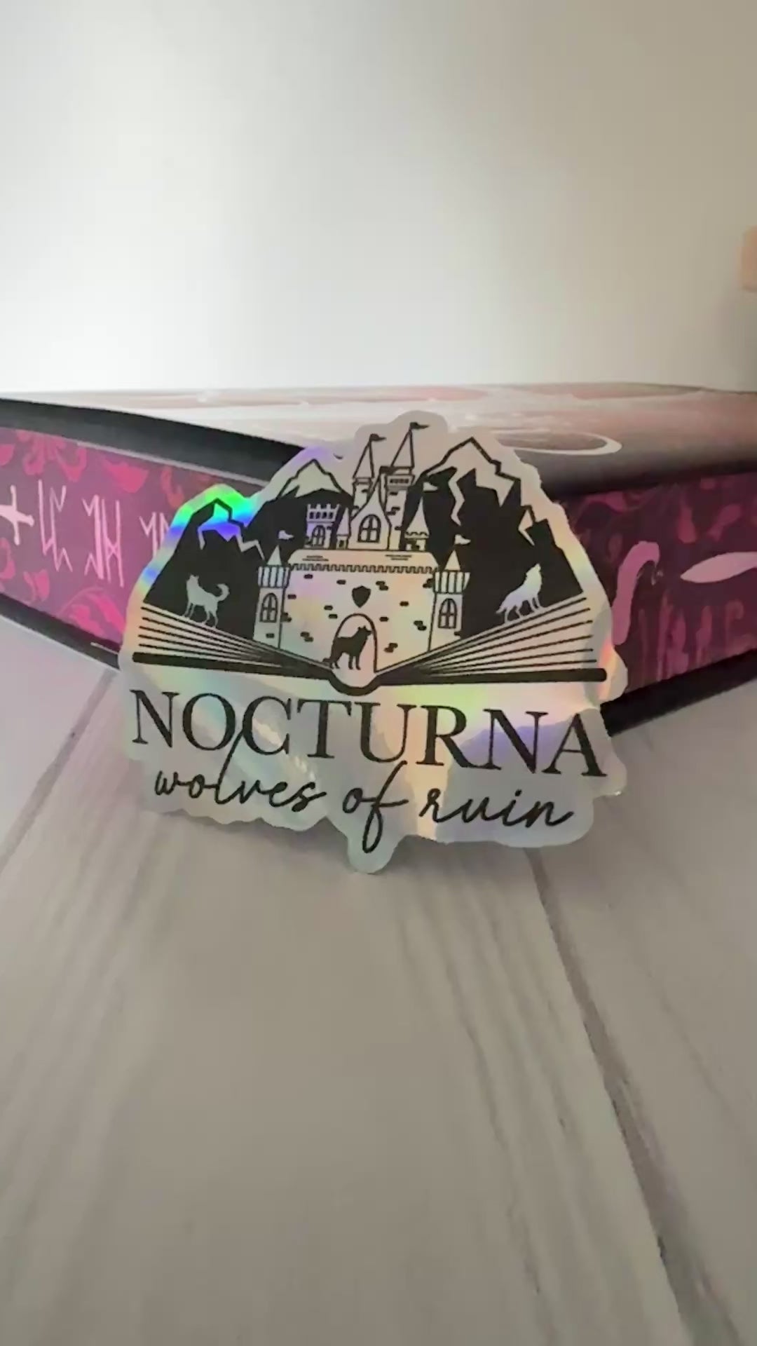 Nocturna holographic sticker featuring an open book with castle, mountains and wolves from Dire Bound
