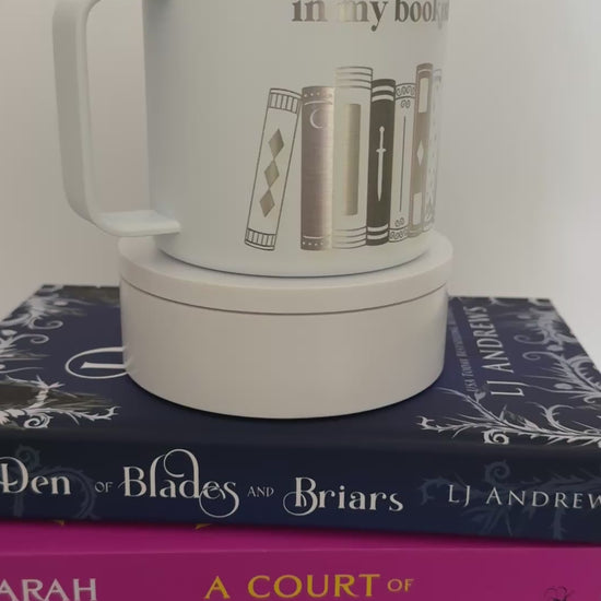 White stainless steel mug with 'in my bookish era' and books engraved around it, set on top of a stack of books.