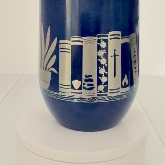 blue wine tumbler spinning around, engraved with "in my bookish era" and books on a book shelf with a dragon