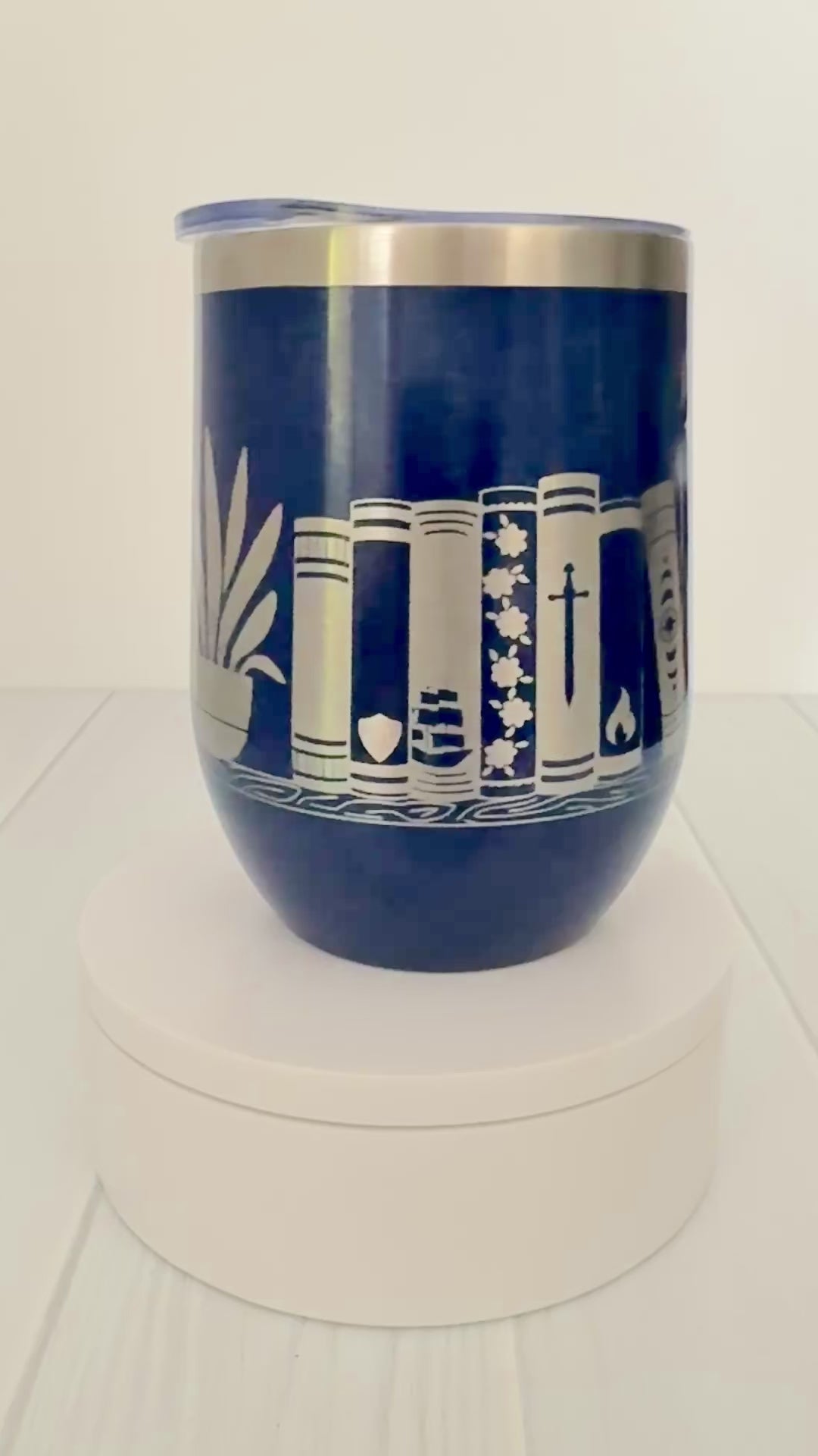 blue wine tumbler spinning around, engraved with "in my bookish era" and books on a book shelf with a dragon