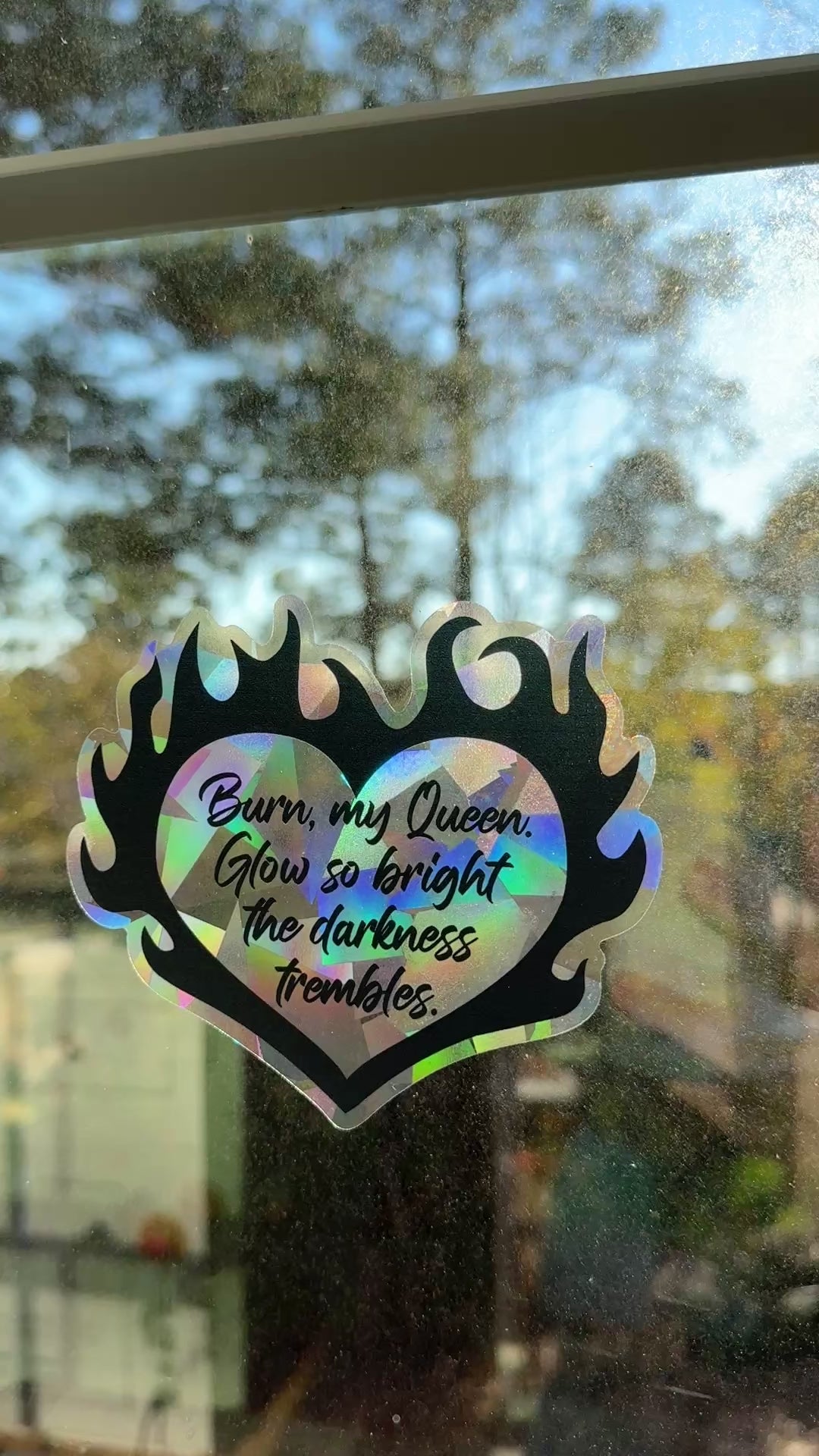 Flaming heart suncatcher decal on a window with the quote "Burn, my Queen. Glow so bright the darkness trembles."
