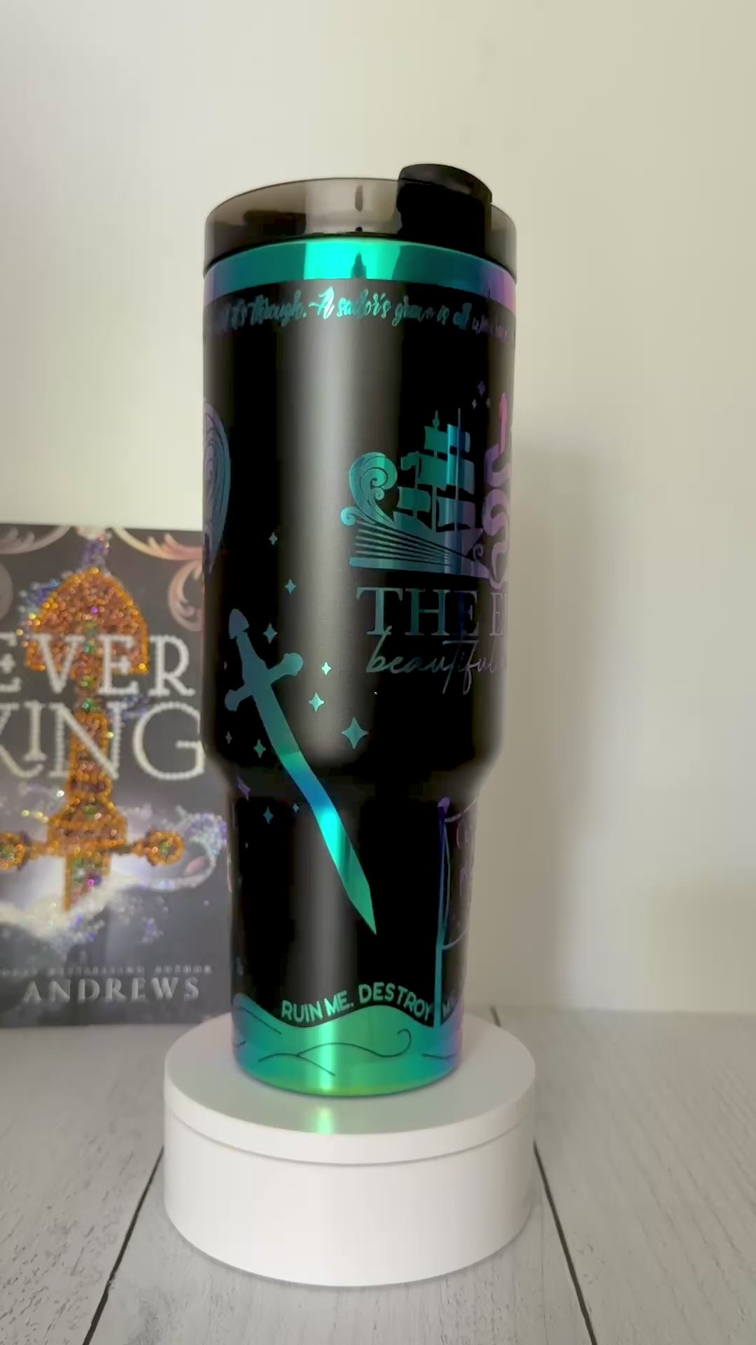 A black Ever King themed tumbler with rainbow engraved details from the books by LJ Andrews including a heart made of waves that says 'hello love' and an open book design with ship, serpent and songbird that says 'the Ever: beautiful monster'